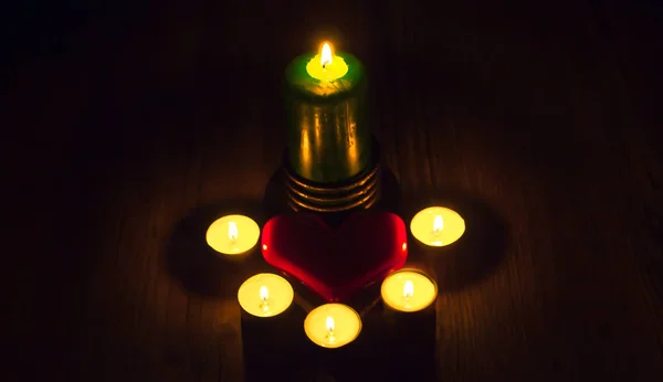 Ein rotes Herz liegt zwischen den Kerzen auf einem Holztisch. Geschenke — Stockfoto