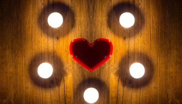 Ein rotes Herz liegt zwischen den Kerzen auf einem Holztisch. Geschenke — Stockfoto