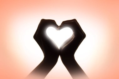 Hands depicting a heart on a pink background in pastel colors. S