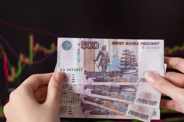 Hands holding Russian rubles in front of a computer monitor with the currency market and Forex trading chart. Trading stocks, bonds, and securities on the stock exchange. Trader in Russia with ruble.