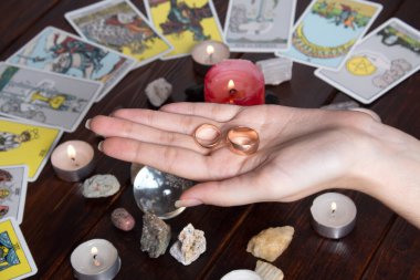 Bangkok, Tayland, 15.20 Mart. Kız elinde Tarot kartları, kristaller, sihirli bir top ve yanan bir mum ile evlilik yüzükleri tutuyor. Fal bakımı ve aşk ayini, aşk büyüsü.