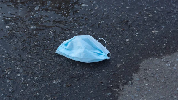 A protective medical face mask is lying on the muddy ground. Mask for protection from the flu epidemic, viruses and coronavirus.