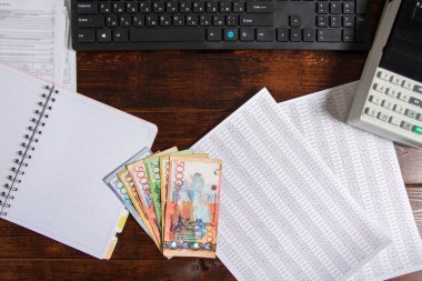 Bilgisayarın, not defterinin ve belgelerin yanındaki masada KZT 'nin onluğu var. Kağıt banknotlar KZT 'yi gerer. Kazakistan Bankası