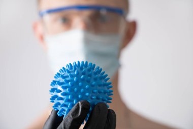 Koruyucu gözlük, tıbbi maske ve siyah eldiven takan bir doktor virüsün bir kopyasını elinde tutuyor..