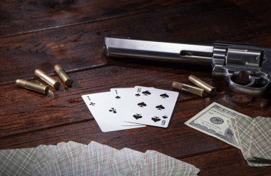 Kumarda, pokerde ya da 21 'de para için. Tahta bir masada fişekli bir tabanca, nakit paralar ve maça ası ve altılı bir deste iskambil kağıdı var. Tehlikeli kumar borçları