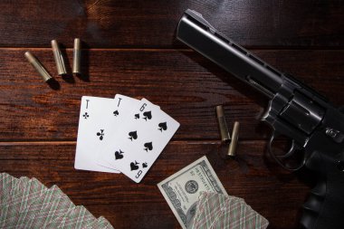 Kumarda, pokerde ya da 21 'de para için. Tahta bir masada fişekli bir tabanca, nakit paralar ve maça ası ve altılı bir deste iskambil kağıdı var. Tehlikeli kumar borçları
