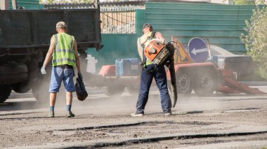 Bir işçi tozu patlatır ve yola zifti döker. Yol işe yarar. İşçiler yol yüzeyini onarıp sokağı asfaltlıyorlar. Tulumlu ve kürekli insanlar yollara toprak atıp delikleri dolduruyor..