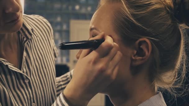 Artista de maquillaje profesional poniendo cosméticos en la cara modelo rubia — Vídeos de Stock