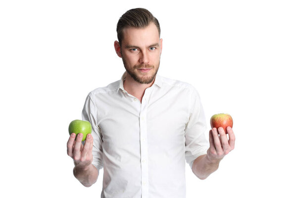 Focused man in a white shirt holding two apples, one green and one red, looking at camera. White background.