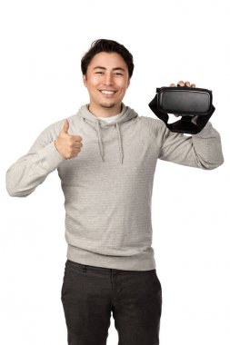 Yüzünde kocaman bir gülümseme ile VR gözlük tutan bir gri kapüşonlu serin adam. Beyaz arka plan.