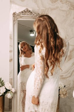 Gelinlik içinde güzel bir gelin. Zarif beyaz elbiseli gelin aynaya bakıyor. Gelin hazırlıklarının sabahı.