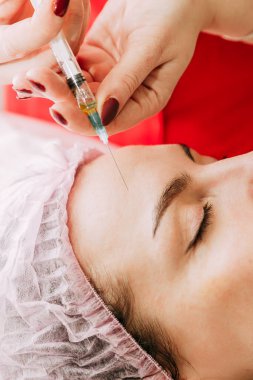 Kadın alnına botoks yapan uzman güzellik uzmanının ellerini kapatın..