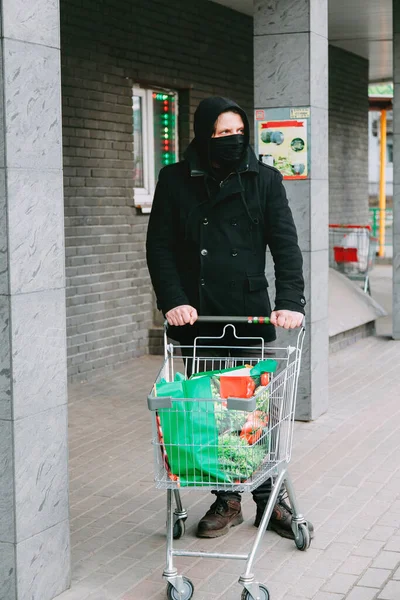 Ein Mann kommt mit Einkäufen vom Einkaufen mit Mundschutz nach Hause, um die Ausbreitung des Coronavirus einzudämmen — Stockfoto