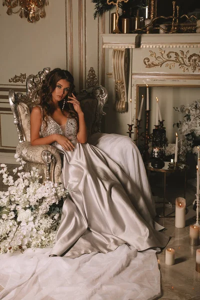 Lüks elbiseli muhteşem genç kadın, yanan mumlarla lüks bir dairede bir sandalyede oturuyor. — Stok fotoğraf