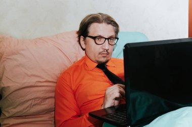 Yatak odasında dizüstü bilgisayarı olan bir adam. Karantina ve kendini izole etme süresince evden çalış. Karantina, salgın hastalık, koronavirüs, online çalışma, eğitim, maket. Evde kal.
