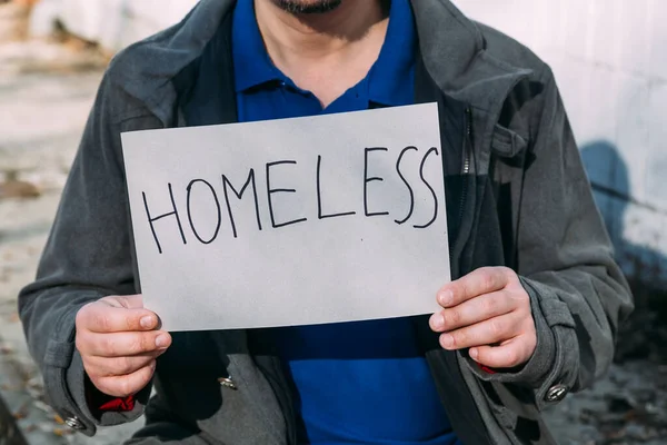 misery man sitting on garbage dump and holding piece of cardboard with homeless inscription