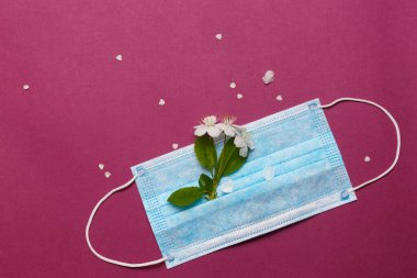 Beyaz çiçekli ve yeşil yapraklı tıbbi maske. Metnin altına yerleştir. Covid-19 salgını bağlamında bahar ve yaz kavramı. Alerji konsepti.