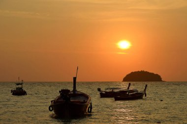 Bir tekne bir kızıl gökyüzü ve tropikal günbatımı karşı silüeti