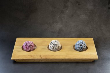 Tahta tepside, koyu gri arka planda üç farklı kalori ev yapımı vegan enerji topları.