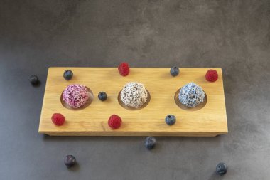 Üç farklı kalorili ev yapımı vegan enerji topları, ahşap tepside, koyu gri arka plan, ahududu ve yaban mersini.