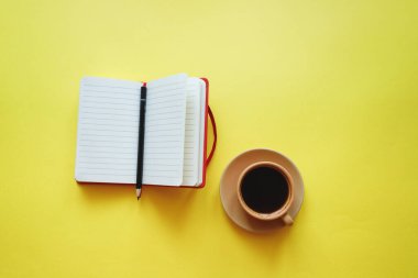 Sarı arka planda not defterli bir fincan kahve.