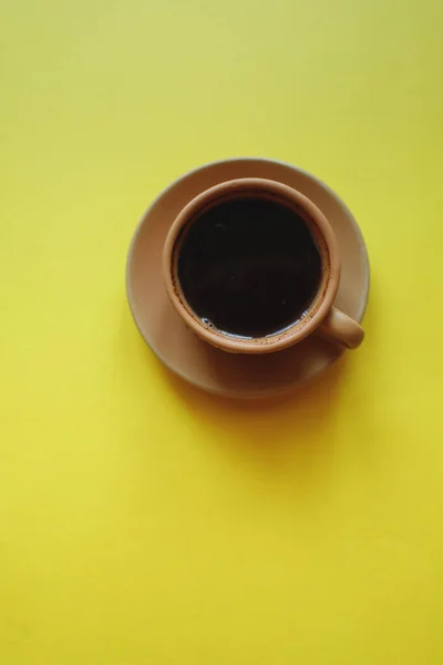 Sarı arka planda not defterli bir fincan kahve.
