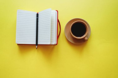 Sarı arka planda not defterli bir fincan kahve.