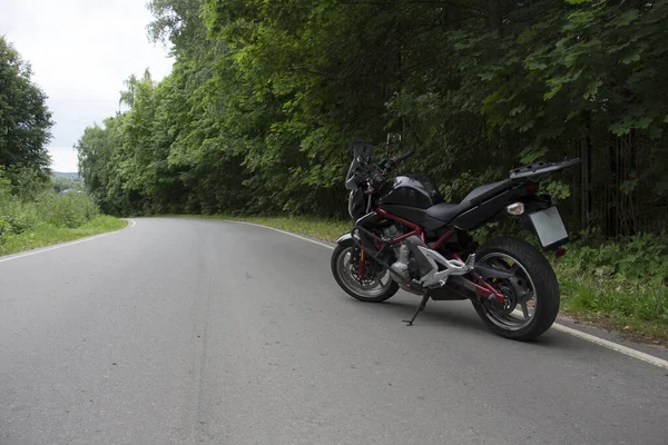 Řidič na koni motocyklu na asfaltové silnici lesem. — Stock fotografie