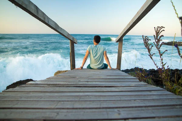 Мужчина, сидящий на деревянном мосту на берегу моря — стоковое фото