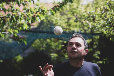 Kırklı yaşlardaki bir adam yeşil bir zeminde su sarmalı yapan bir topu fırlatır ve döndürür.