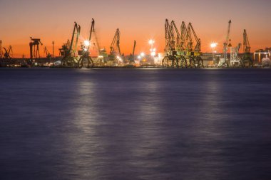 Gün batımında, ışık yansıması ile endüstriyel vinçleri olan gemi limanı