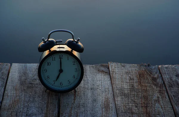 Concepto horario de verano. Reloj despertador en puente de madera sobre fondo de salida del sol del mar — Foto de Stock