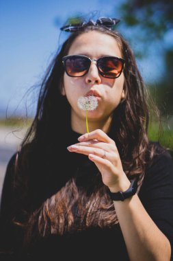 Kafkasyalı bir kız bulutlu, parlak bir günde karahindiba üflüyor. Tasasız mutluluk kavramı.