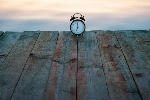 Concepto horario de verano. Reloj despertador en puente de madera sobre fondo de salida del sol del mar —  Fotos de Stock