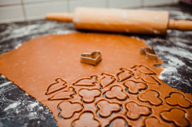 Kara hamurlar, rulo, baharatlar ve kurabiye kesicilerle Noel için pişirme. Zencefilli bisküvi tarifi. Kurabiyeler fırında pişirmeye hazır. Masada un kaplı çiğ kurabiyeler var.. 