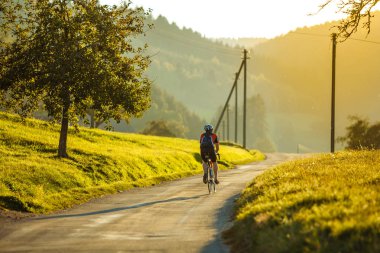 Erkek tam donanımlı bisikletçi gün batımında Almanya 'nın kırsal kesimindeki boş yolda bisiklet sürüyor..