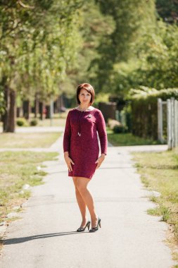 Güneşli bir yaz öğleden sonrasında parkta kısa kırmızı elbiseli genç bir kadın.