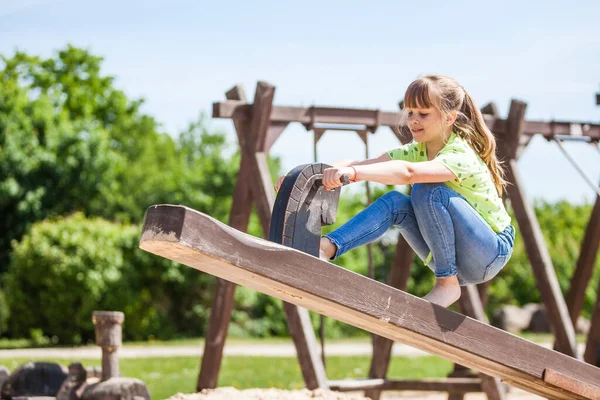 Portrait of little smiling girl child playing outdoor in park in children playground.  Lifestyle natural shot with blurred background. Wooden outdoor playground equipment that is guaranteed to last outdoors in childhood education centre.