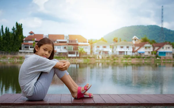 Gadis cantik duduk di dekat kolam alami dengan perumahan . — Stok Foto