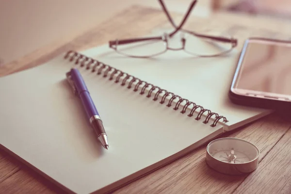 Pen, notebook, kompas, glazen en mobiele telefoon op houten tafel — Stockfoto