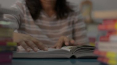 Kız sayfayı çevirir ve evdeki masanın üstünde kitap yığını olan bir ders kitabı okur. Eğitim kavramı.
