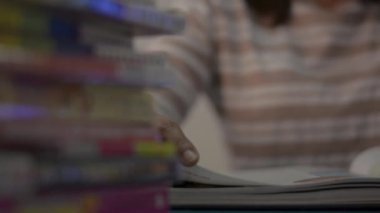 Kız sayfayı çevirir ve evdeki masanın üstünde kitap yığını olan bir ders kitabı okur. Eğitim konsepti. Döndürme çekimi.