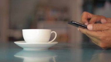 İş adamı masada akıllı telefon kullanıyor ve evde bir fincan kahve içiyor, cep telefonuna mesaj yazıyor..
