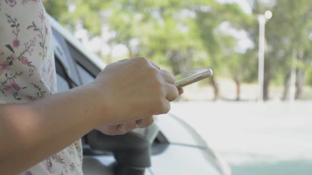 公共の公園で車の近くの社会的なコミュニケーションのための携帯電話を使用して女性の手を閉じる — ストック動画