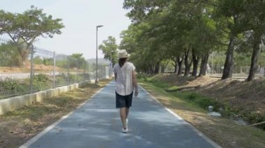 Hasır şapka takan Asyalı kadının arkadan görünüşü yaz boyunca halk parkında yürüyor..