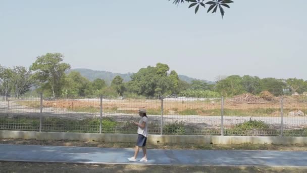 Азиатка Повседневной Одежде Ходит Дороге Пользуясь Мобильным Телефоном Общественном Парке — стоковое видео