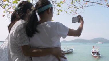  Mother and her daughter posing for selfie together at the pier during summer. Expression of love between mother and daughter.