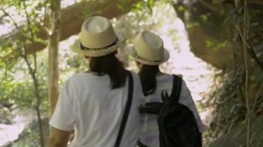 Rear view of mother and her daughter are walking hand in hand together on hiking trail along together in tropical rain forest in thailand.