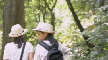 Rear view of mother and her daughter are walking hand in hand together on hiking trail along together in tropical rain forest in thailand.