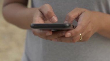 Kadın eli kapalı cep telefonundan mesaj yolluyor iletişim için ve internette sohbet için. Sıradan giyinmiş bir kadın cep telefonu kullanıyor ve parkta yürüyor..
